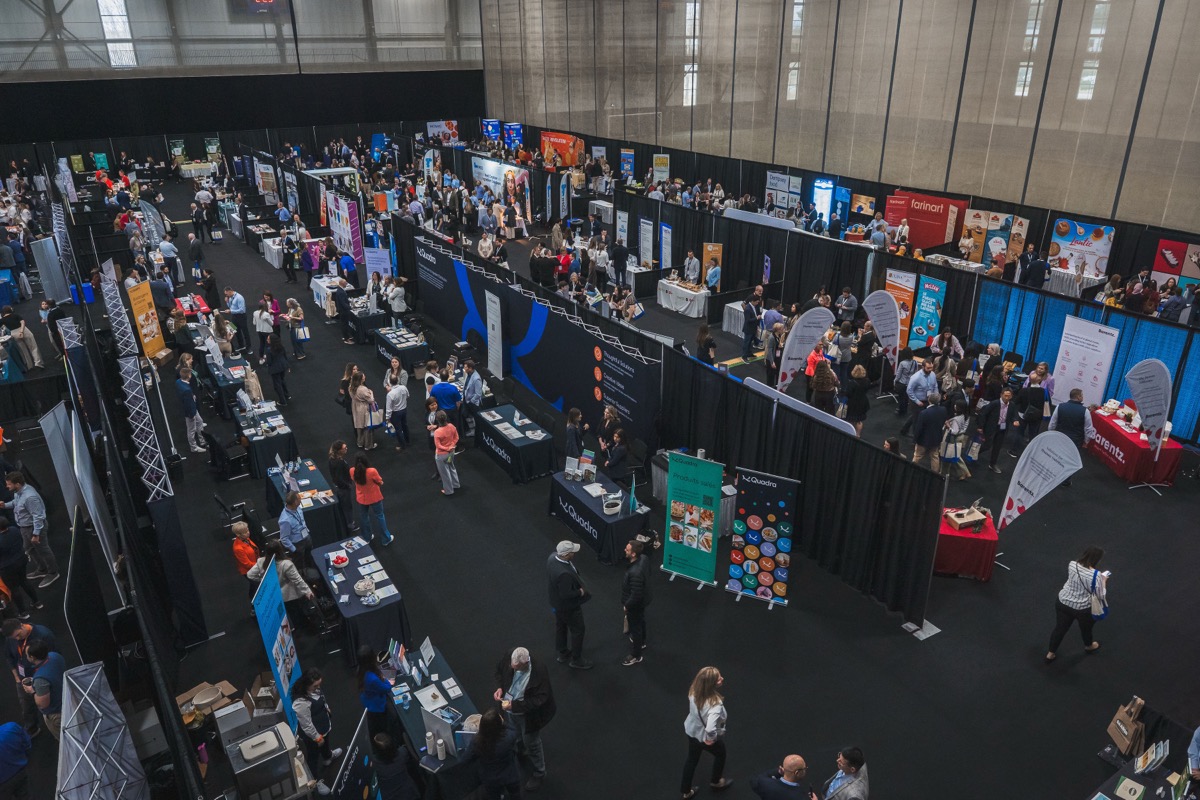 Allées animées du salon avec visiteurs découvrant les kiosques des fournisseurs